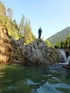 Person in Neoprenanzug steht auf Felsen über einem Fluss mit Wasserfall.
