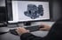 Hände tippen auf einer Tastatur vor einem Computermonitor, der ein 3D-Modell einer komplexen Maschinenkomponente anzeigt.