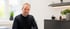 Ein Mann mit kurzen grauen Haaren und Bart in einem schwarzen Pullover sitzt in einem hellen, modern eingerichteten Büro.