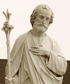 Sepia-toned statue of Saint Joseph with a beard, holding a staff with lilies, hand over his chest.