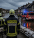 Feuerwehrmann mit "FEUERWEHR HOCHWASSER-EINSATZ" auf dem Rücken blickt auf eine überflutete Straße mit Einsatzfahrzeug - Bevölkerungsschutz-Software Notfall- und Krisenmanager (NKM®).