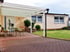 Haus mit weißem Carport, gepflasterter Einfahrt, grüner Wiese und Gartenmöbeln vor der Haustür.