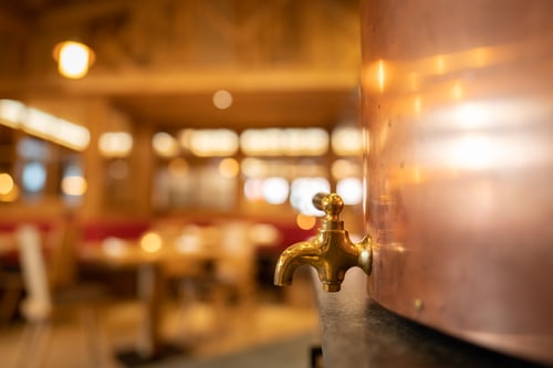 Messing-Zapfhahn am kupfernen Braukessel der Hausbrauerei Goldener Adler, dahinter die Wirtshausstube