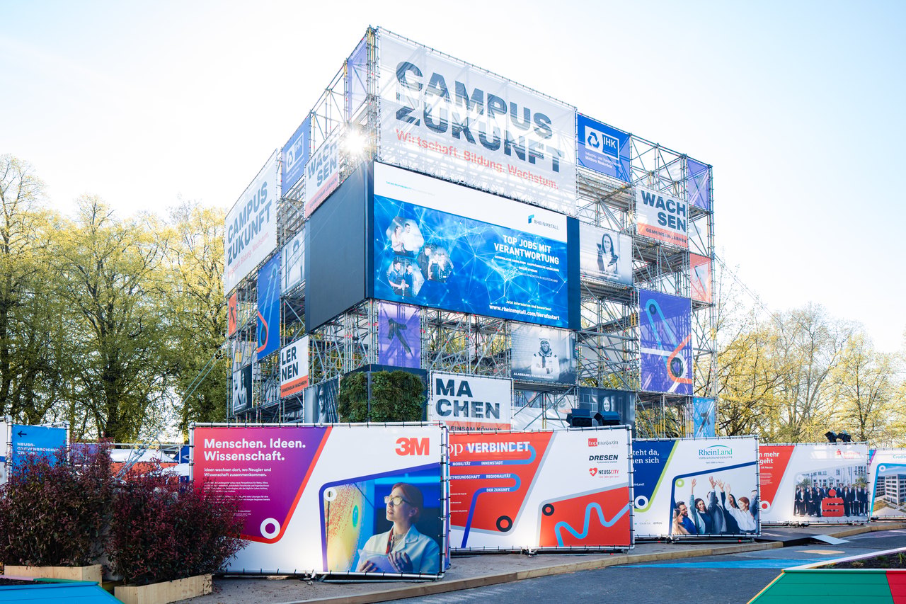 Der vollständig aufgebaute Campus-Zukunft-Pavillon – mehretagige Gerüstarchitektur mit großflächigen Partnerbannern und LED-Displays
