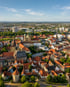 Luftaufnahme der Altstadt von Osnabrück mit dem Dom St. Peter, roten Ziegeldächern und grünen Bäumen unter blauem Himmel.