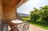 Terrasse mit Holzwand, Tisch, Stühlen, Blick auf grüne Wiese und Berge unter einem Sonnensegel.