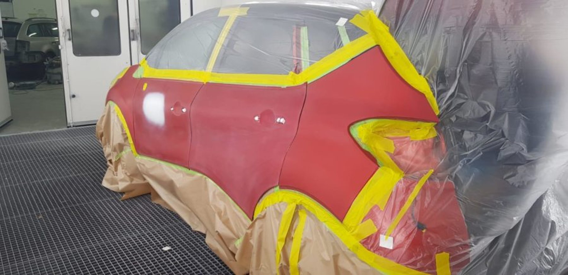 Teilflächig abgeklebte rote Fahrzeugtür in der Lackierkabine vor der Lackierung