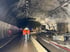 Männer in Warnwesten stehen in einem verrauchten Tunnel vor einem ausgebrannten LKW-Wrack und einem roten Schlauch.