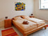 Schlafzimmer mit zwei Einzelbetten, zwei Nachttischen, orangefarbenen Teppichen und einem farbigen Kunstwerk.