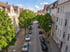 Wohnstraße mit Kopfsteinpflaster, geparkten Autos und grünen Laubbäumen zwischen historischen Stadthäusern bei Tageslicht.