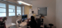 Eine Frau sitzt an einem modernen Empfangstresen mit Computerbildschirm in einer hellen Arztpraxis oder einem Büro.