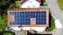 Dach eines Einfamilienhauses mit zahlreichen blauen Solarmodulen und zwei Dachfenstern. Daneben steht ein weißes Auto.