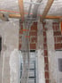 Graue Kabelstränge und orangefarbene Kabelbinder führen zu einem Unterputz-Sicherungskasten in einer Rohbauwand.