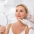 A woman in a white top receives a facial injection in a brightly lit room.
