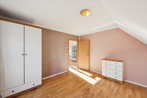 Leeres Dachzimmer mit weißem Schrank, Kommode und Holzboden.