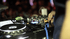 Animiertes GIF einer DJ-Konsole, bei der ein DJ Regler und Knöpfe bedient, während bunte Lichter im Hintergrund aufleuchten in Ialien