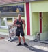 Daniel Wunderlich in schwarzer Sportkleidung zeigt auf das Schild "Exclusiv Fit" eines Fitnesscenters.