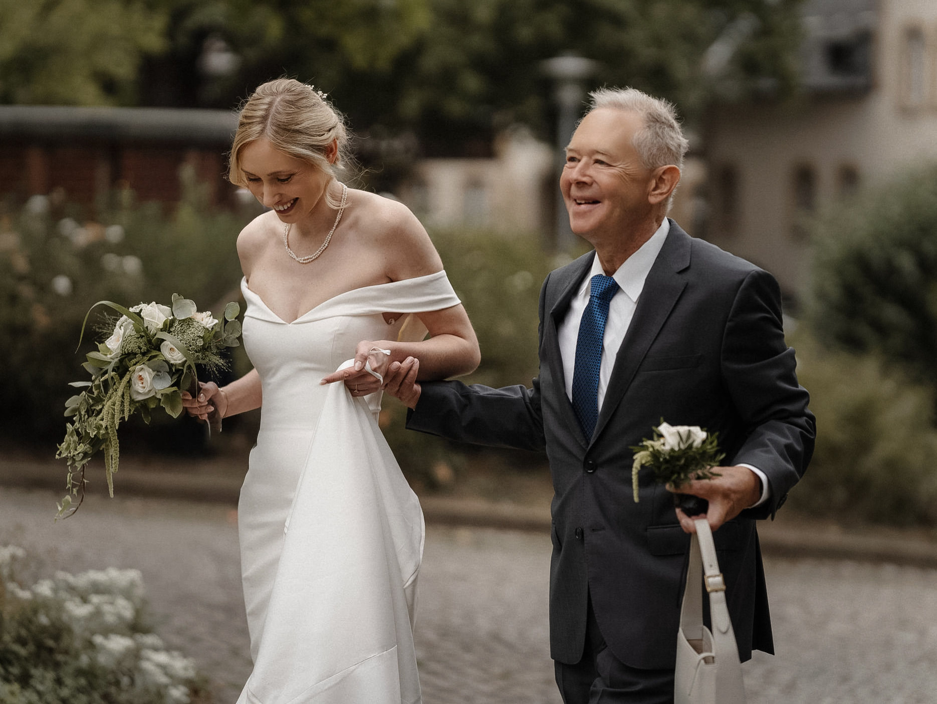 Brautvater und Braut gehen lachend Arm in Arm am Schloss Eller in Düsseldorf.