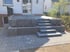 Moderne Terrasse aus grauen Steinplatten mit integrierten Pflanzkübeln und einer breiten Blockstufentreppe zum Garten.