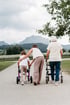 Eine Frau, ein Kind und eine Seniorin gehen mit Rollatoren auf einem Weg vor einer Bergkulisse spazieren.
