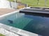 Ein moderner Gartenpool mit dunkler Auskleidung, Steineinfassung und angrenzender Holzterrasse vor einer Rasenfläche.