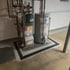 A furnace and water heater stand on a gray concrete slab surrounded by a black grated drain in a basement.
