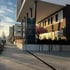 Gebäude mit schwarzem Schild "Büro & Coworking" und "10", rosafarbenem Baum daneben, Gehweg und geparkten Autos.