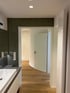 Modernes Badezimmer mit Waschtisch, dunkler Wand und offenem Durchgang zu einem Flur mit Holzboden.