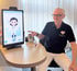 Arzt zeigt auf einen Bildschirm mit Cartoon-Ärztin und Herz-Logo auf seinem Hemd.
