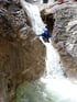 Person in Neoprenanzug und Helm klettert einen Wasserfall in einer Felsenschlucht hinab.