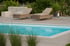Zwei beige Sonnenliegen stehen auf einer Holzterrasse neben einem Swimmingpool mit blauem Wasser und grüner Bepflanzung.