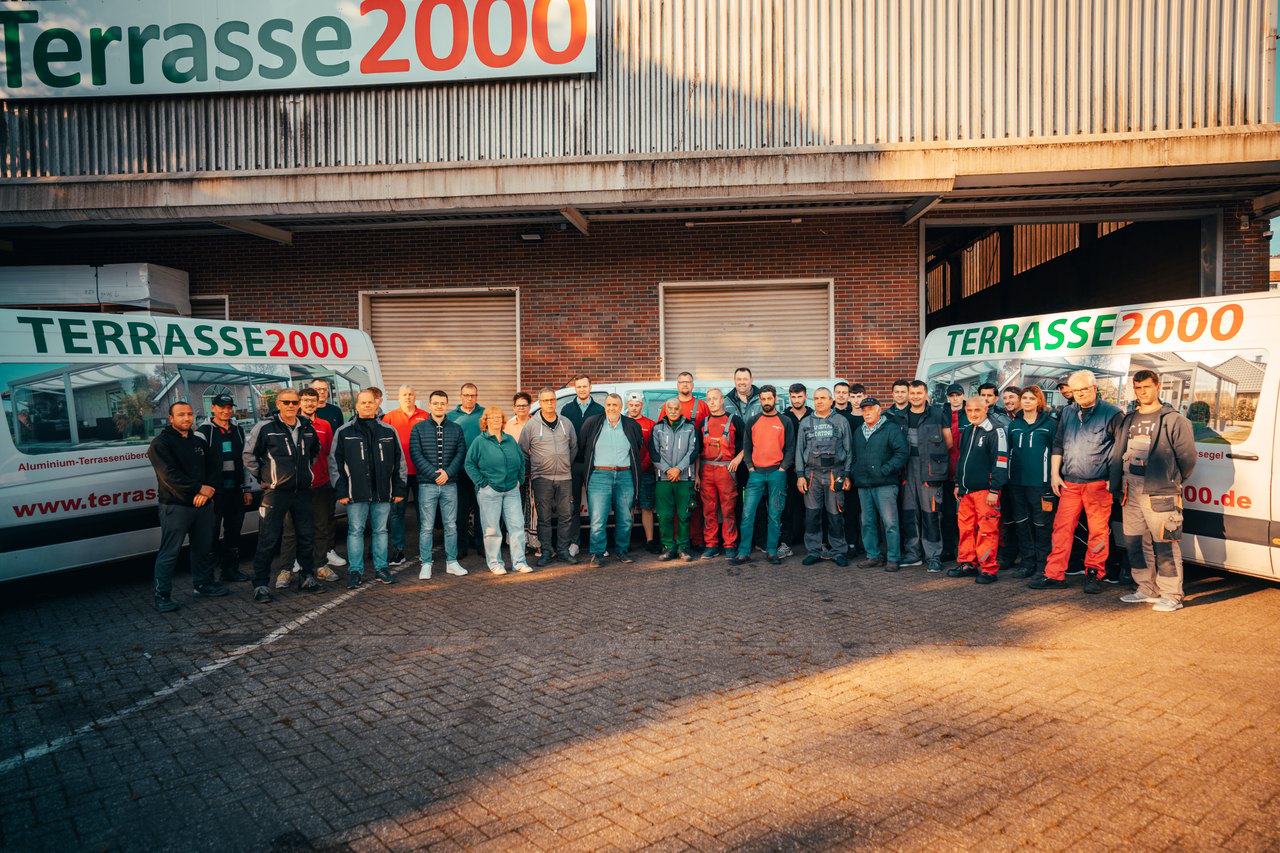 Das Team von Terrasse 2000 vor Firmenfahrzeugen und dem Firmengebäude