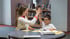 Eine lächelnde Lehrerin und ein Junge geben sich im Klassenzimmer ein High-Five über einem runden Tisch.