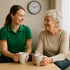 Eine Alltagsbegleiterin sitzt mit einer Seniorin bei Kaffee in einem Wohnzimmer in Wilhelmshaven. Beide lachen entspannt, Entlastung im Alltag