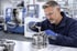 Ein Ingenieur in Schutzbrille und Handschuhen montiert ein Metallteil in einer Fabrik.