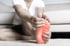 Person sits on rug, clutching foot in pain with red sore area.