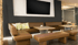 Modernes Wartezimmer mit braunen Ledersofas, Holzbänken, Tischen und großem schwarzen Bildschirm an dunkelgrauer Wand.