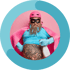 Mann mit rosa Helm, Umhang, blauer Maske, Handschuhen und tätowiertem Bauch, hält Sprühflasche.