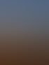 Ein mobiles Bohrgerät steht bei Sonnenuntergang auf einem weiten Acker vor einer bewaldeten Hügelkette.