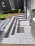 Graue geflieste Treppe mit Metallgeländer führt zu einem Hauseingang mit Rinne und Gitterrost.