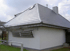 Weißes Einfamilienhaus mit grauem Ziegeldach, Dachfenster, Schornstein und Rankgitter an der Hauswand.