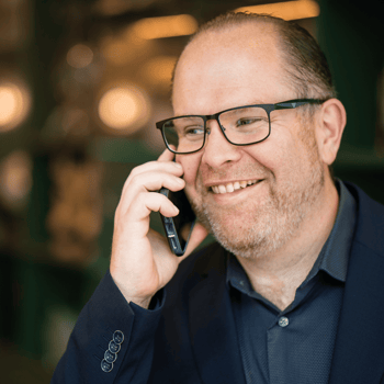 Lächelnder Mann mit Brille und grauem Hemd blickt in die Kamera.