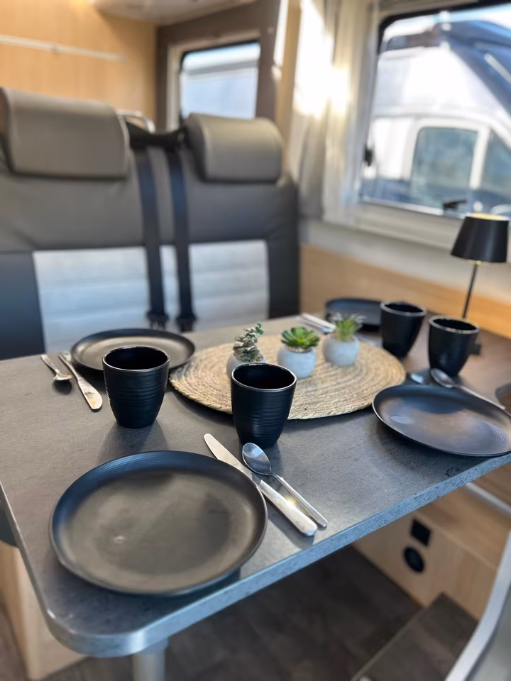 Gedeckter Tisch in einem Wohnmobil mit schwarzen Tellern, Besteck, Tassen und kleinen Pflanzen.