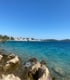 Türkisfarbenes Meer mit Felsen im Vordergrund, einer Küstenlinie mit weißen Gebäuden und Inseln am Horizont unter blauem Himmel mit Sicht aufs Camp Buquz in Kroatien.