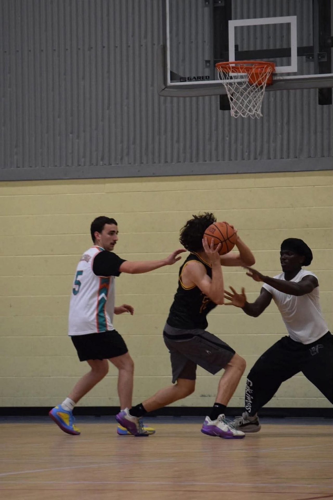 Trois joueurs de basketball se disputent le ballon sous le panier