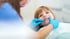 Zahnärztin mit blauen Handschuhen untersucht die Zähne eines lächelnden Kindes in einer Zahnarztpraxis.