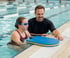 Mädchen mit Schwimmbrille und Lehrer im Schwimmbad, die auf ein blaues Schwimmbrett schauen.