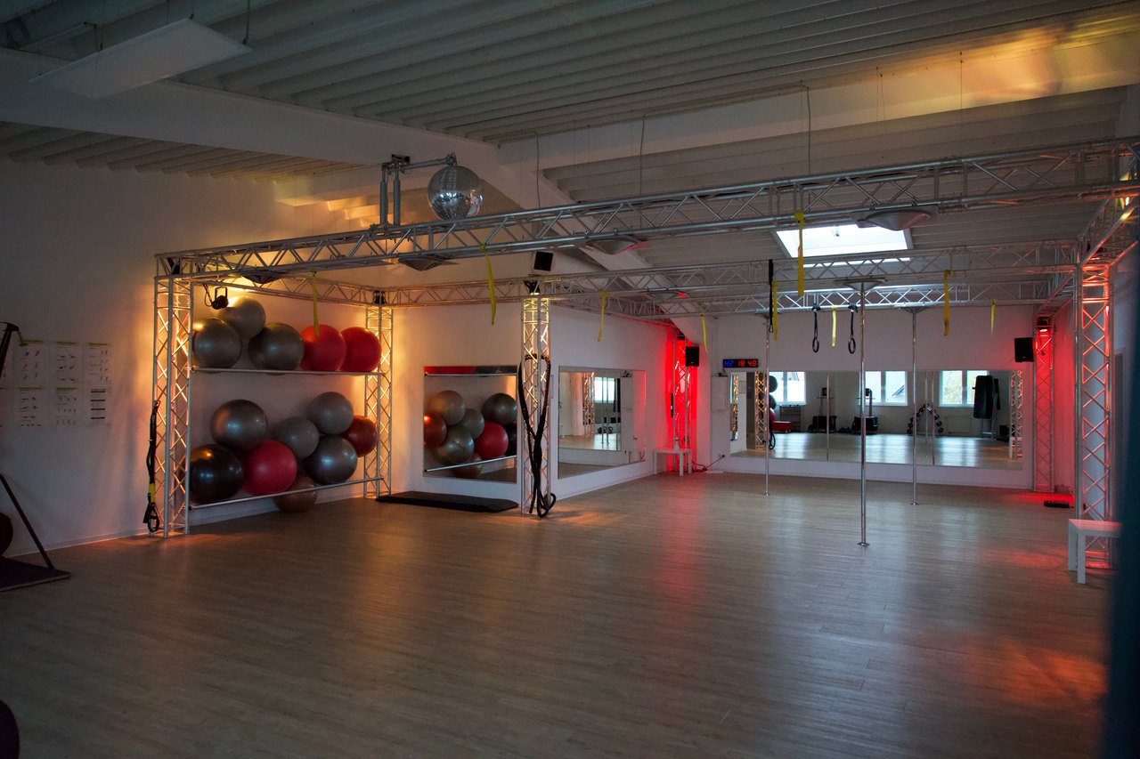 Leeres Fitnessstudio mit Holzboden, Spiegeln und roten Gymnastikbällen.