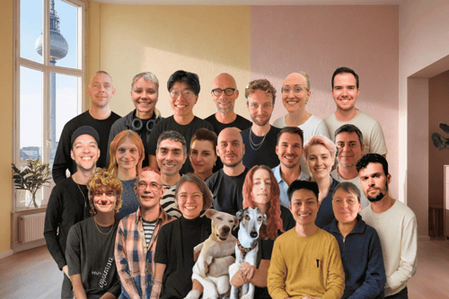 Ein Team von 23 Menschen und einem Hund lächelt vor einer hellen Wand.