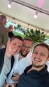 Selfie von drei lachenden Männern bei einer Feier am Abend, im Hintergrund Bäume und eine Zeltdecke mit Strahlern